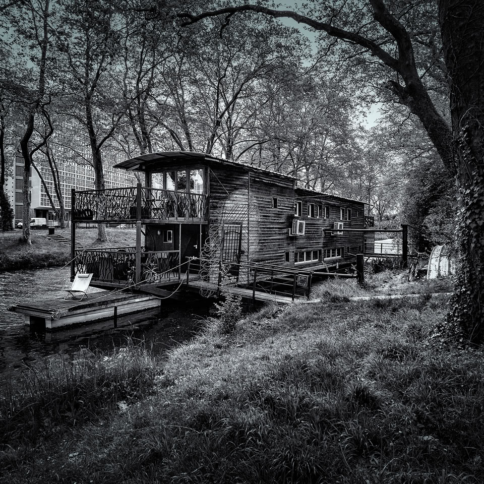 Maison flottante sur un canal bordé d'arbres, avec un petit bateau amarré à côté.