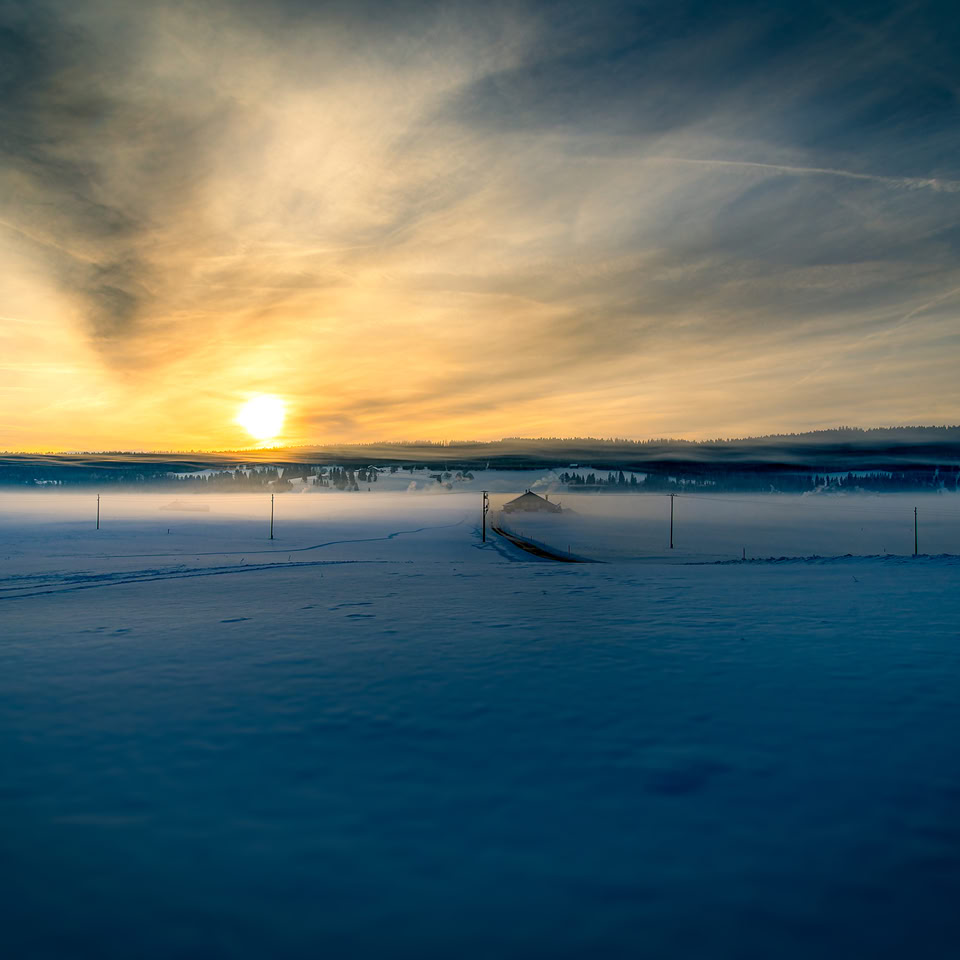 Paysage enneigé au coucher du soleil avec un ciel nuageux et des collines à l'horizon.