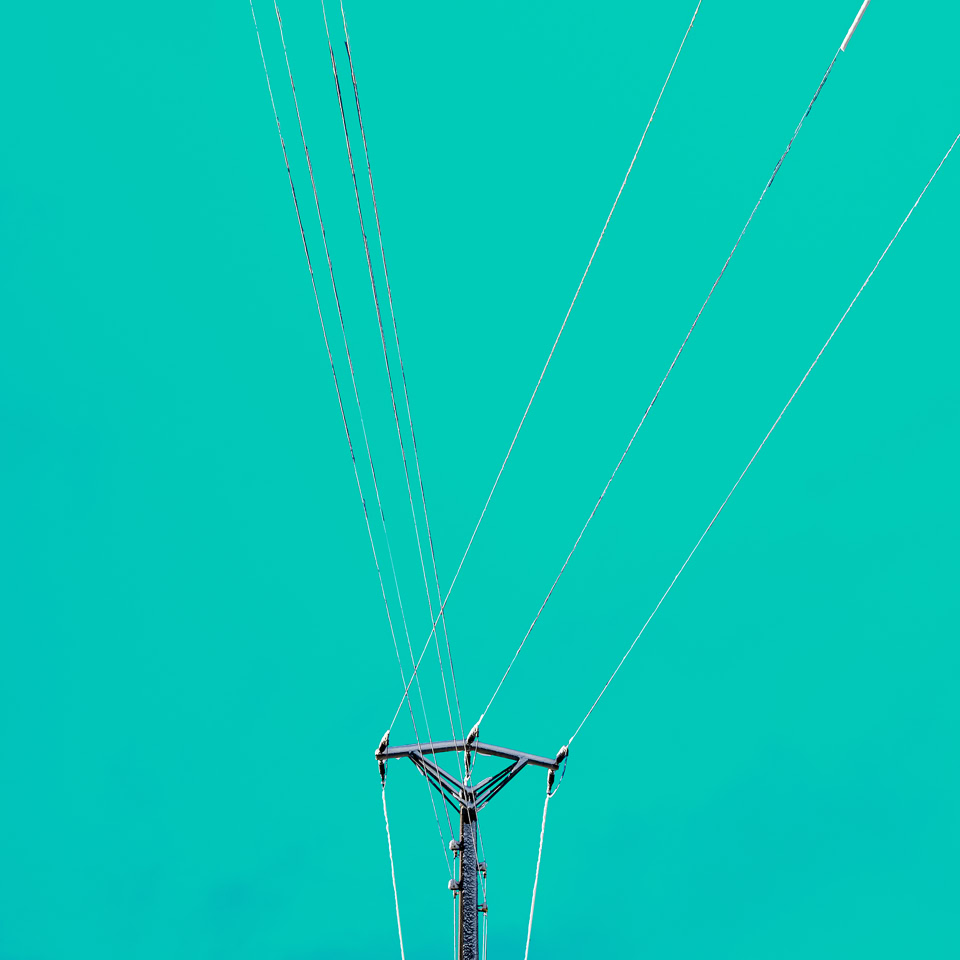 A utility pole with multiple wires extending upwards against a turquoise sky.