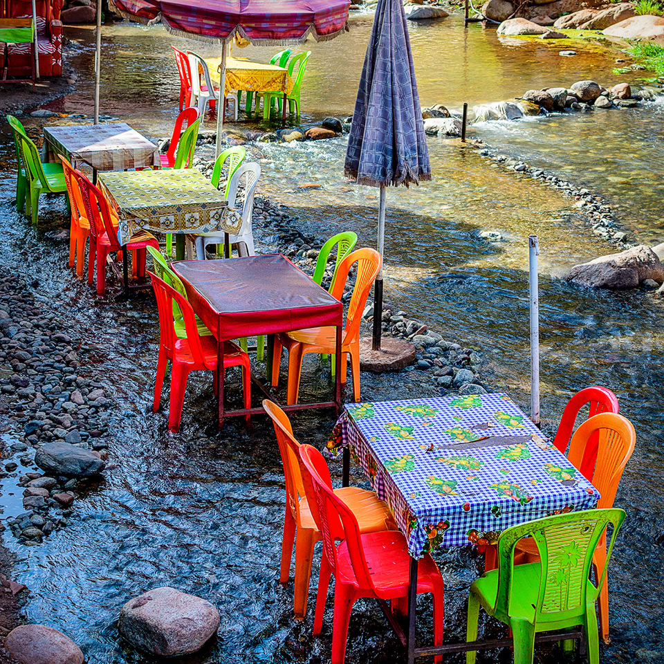 Tables et chaises colorées installées dans un ruisseau peu profond avec des parasols.