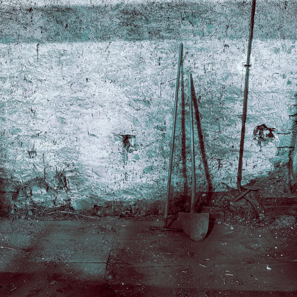 Mur en pierre avec des outils appuyés contre, sol en béton.