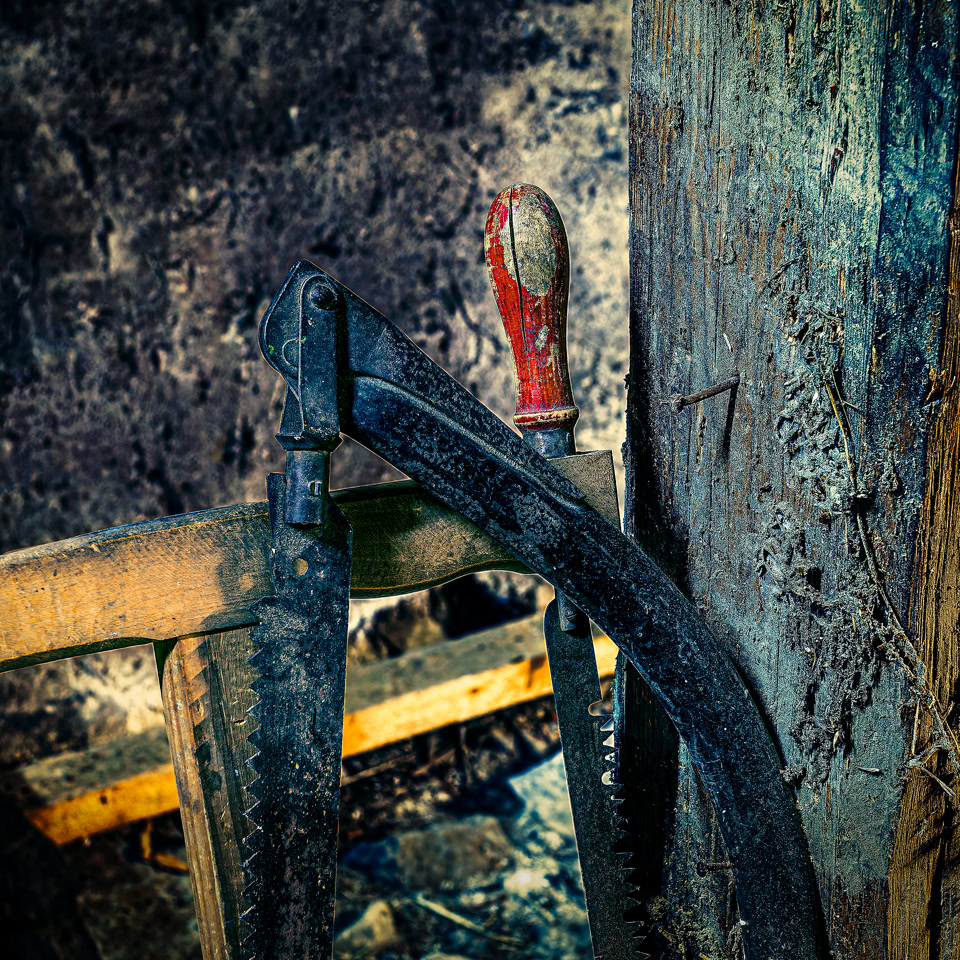 Wood saw leaning against a wooden beam, with a dark wall in the background.