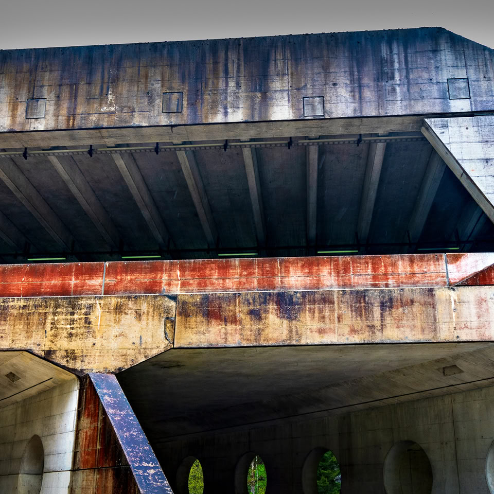 A concrete bridge with visible rust stains and a circular opening, supported by columns.