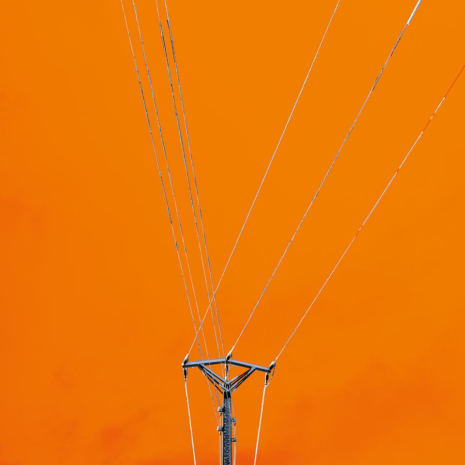 A utility pole with multiple power lines extending upward against a bright orange sky.