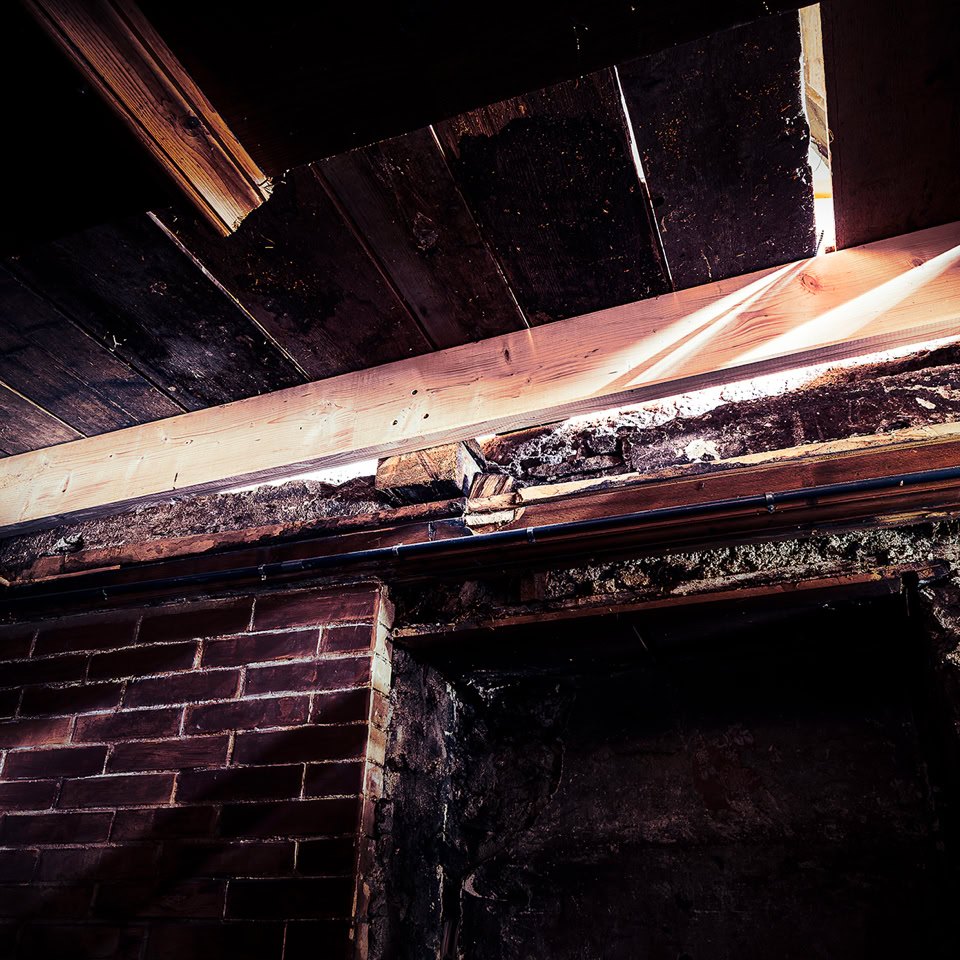 Damaged wooden ceiling with exposed beams and a brick wall.