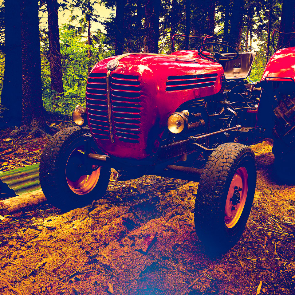 Tracteur rouge sur un chemin forestier avec des arbres en arrière-plan.