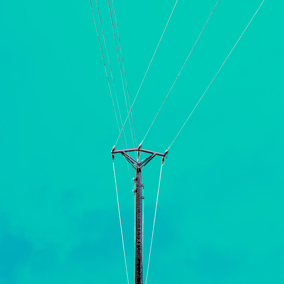 Poteau électrique avec fils contre un ciel bleu turquoise.